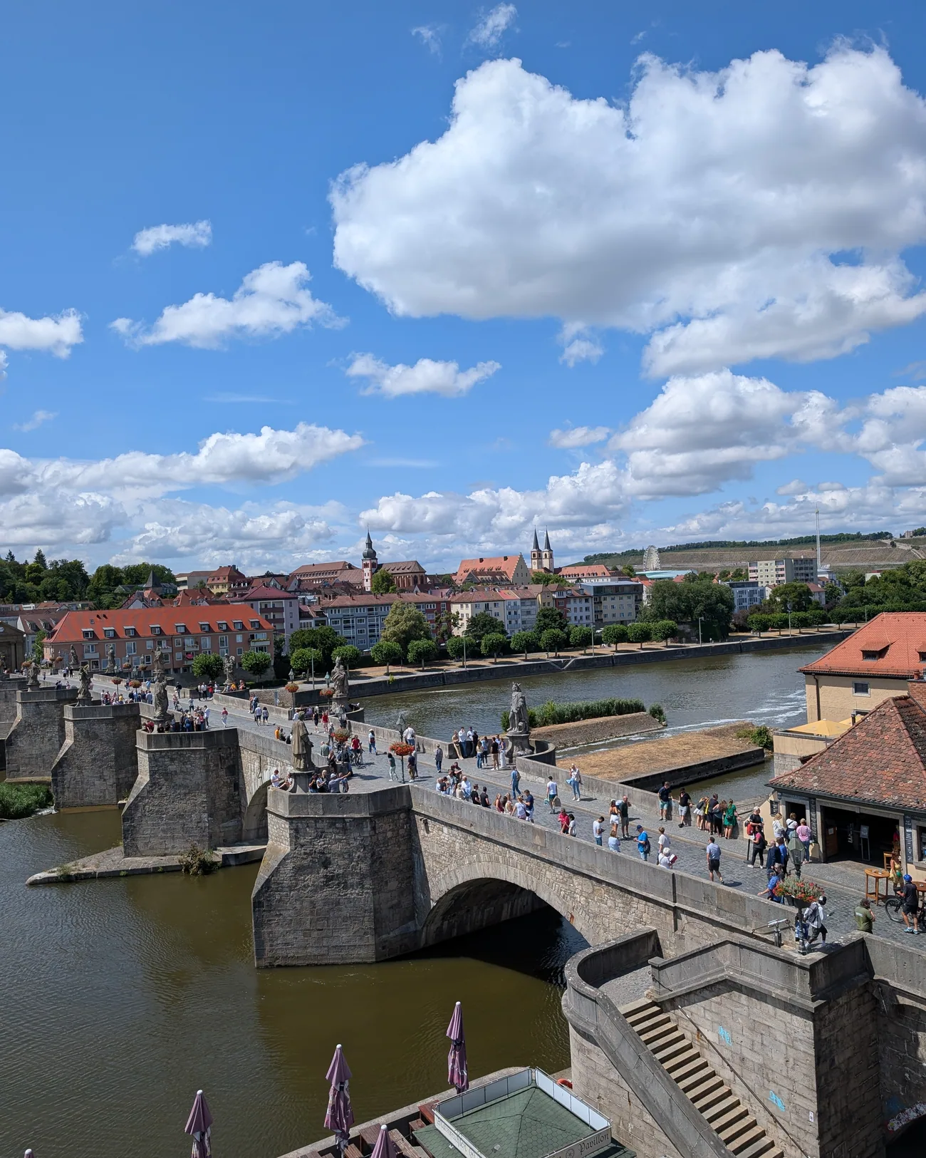 Die Alte Mainbrücke von oben gesehen, Menschen gehen darüber, dahinter die roten Dächer der Altstadt