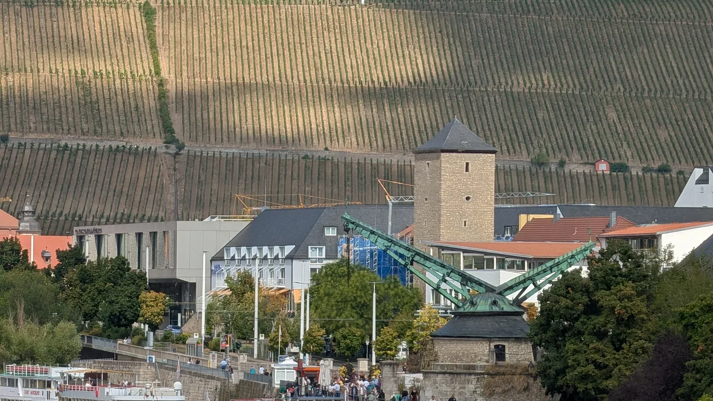 Der Alte Kranen am Mainufer mit den Ausflugsschiffen davor, dahinter die Weinberge am Stein