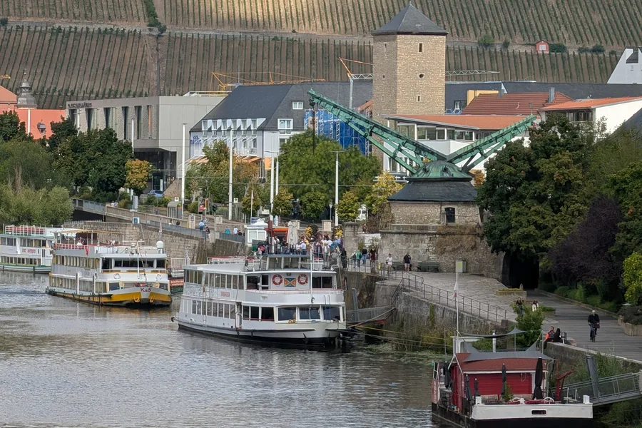 Der Alte Kranen am Mainufer mit den Ausflugsschiffen davor, dahinter die Weinberge am Stein