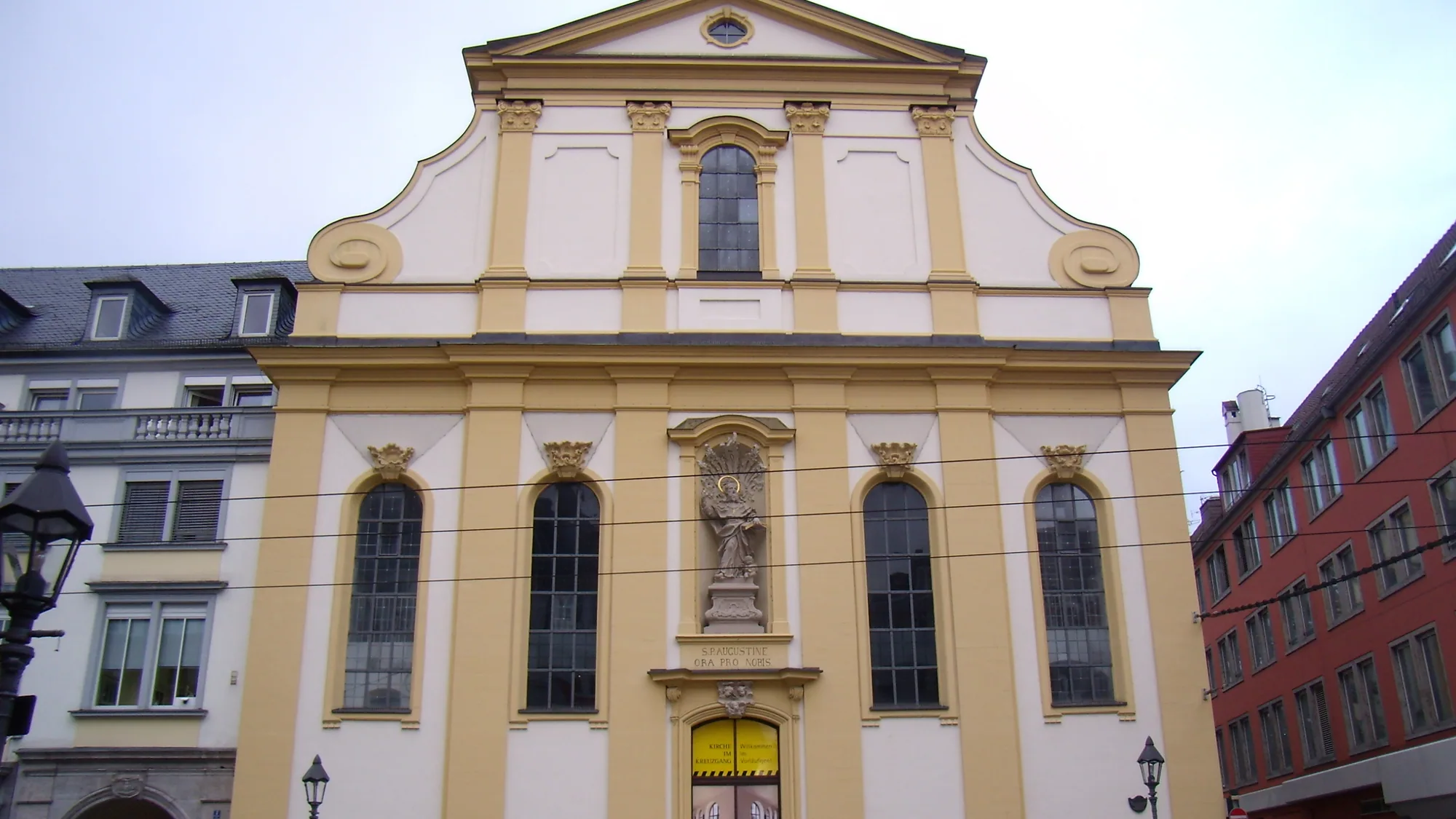 Die Augustinerkirche am Dominikanerplatz, gelb-weiße Fassade mit geschwungenem Giebel und Heiligenfigur über dem Eingang