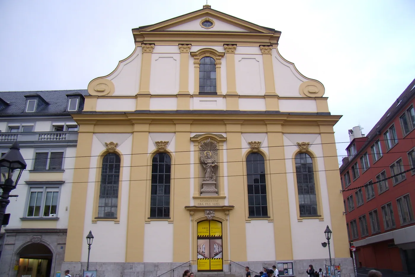 Die Augustinerkirche am Dominikanerplatz, gelb-weiße Fassade mit geschwungenem Giebel und Heiligenfigur über dem Eingang