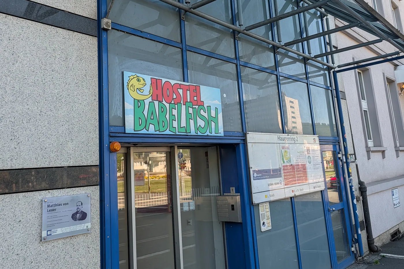 Der Eingang des Hostel Babelfish am Haugerring mit Glasvordach und dem Aushang der Hausnummer 2
