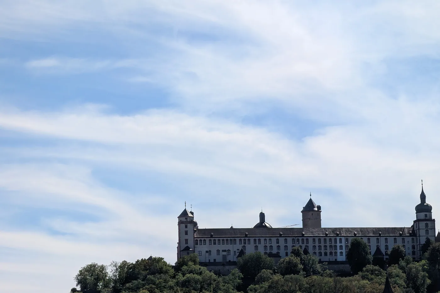 Die Festung Marienberg unter weitem Himmel, die Türme und der lange Bau des Fürstenbaus über den Baumwipfeln