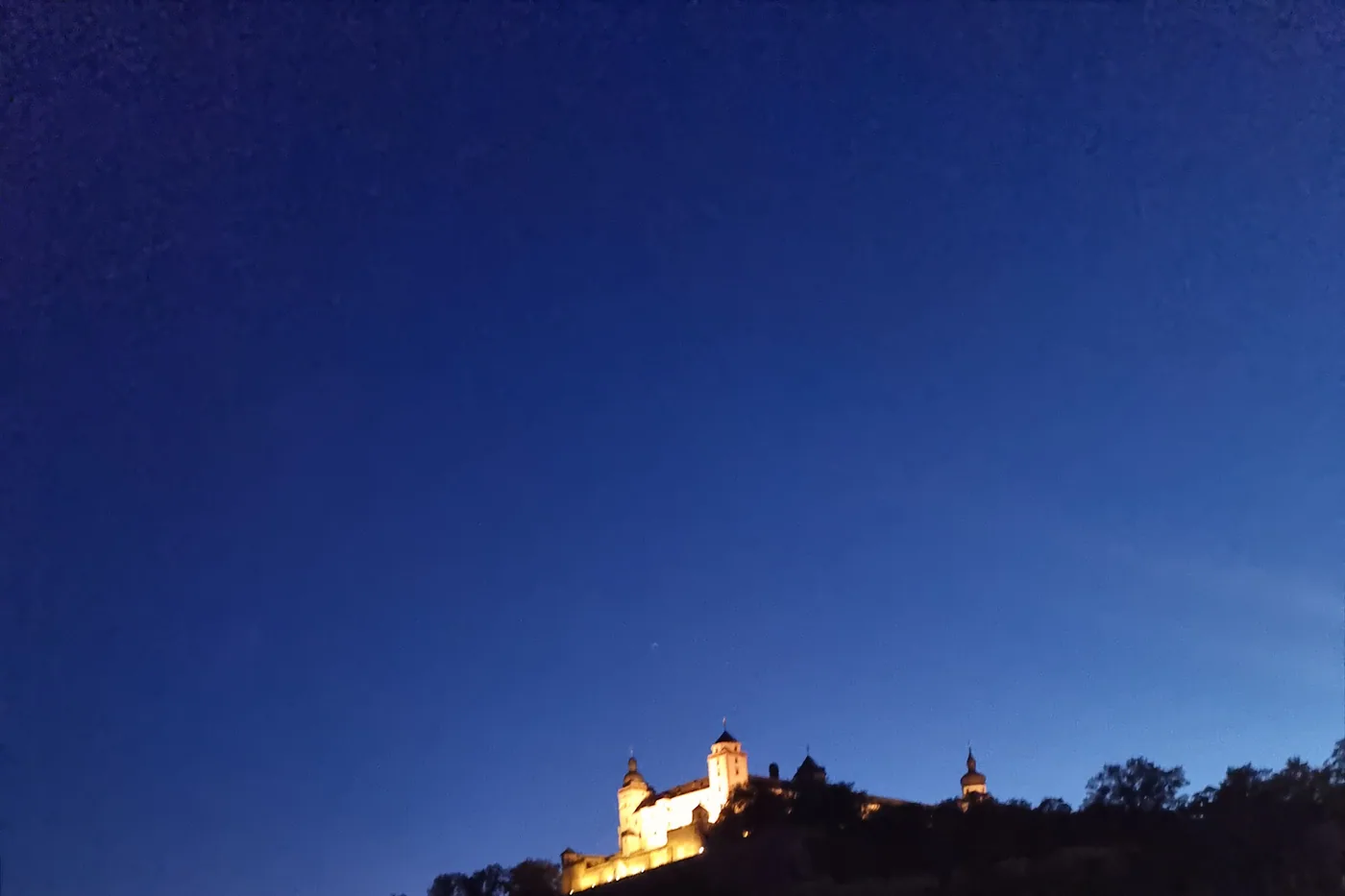 Die beleuchtete Festung Marienberg bei Nacht über dem dunklen Main