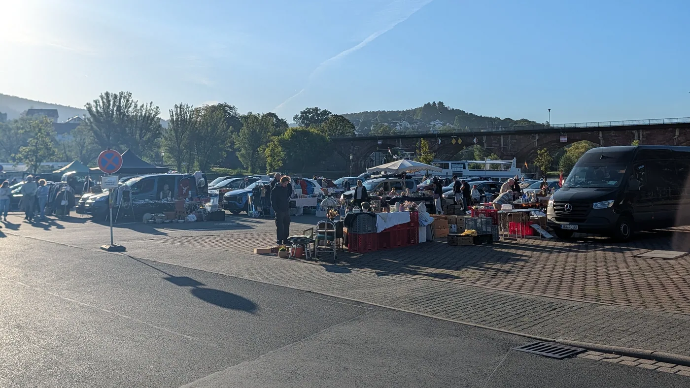 Stände des Flohmarkts auf dem Parkplatz an der Mainbrücke in Lohr, dahinter die Brücke und der Main