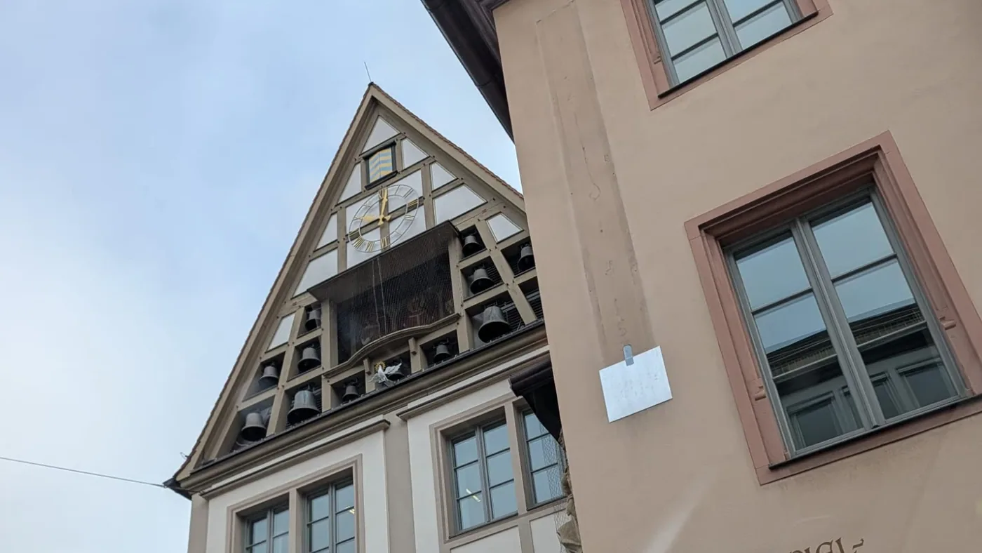 Der Giebel des Bürgerspitals mit Uhr, Glocken und der Drehbühne des Glockenspiels, daneben die Hauswand mit den Spielzeiten