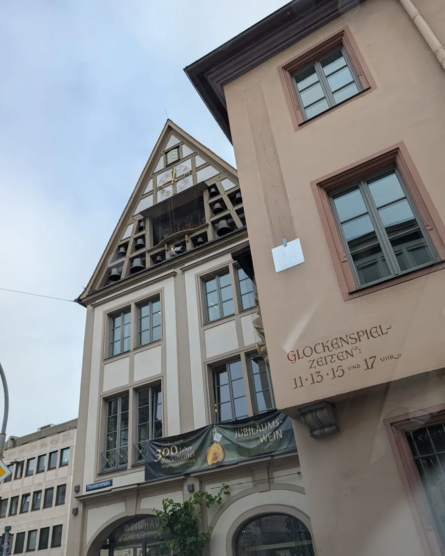 Der Giebel des Bürgerspitals mit Uhr, Glocken und der Drehbühne des Glockenspiels, daneben die Hauswand mit den Spielzeiten
