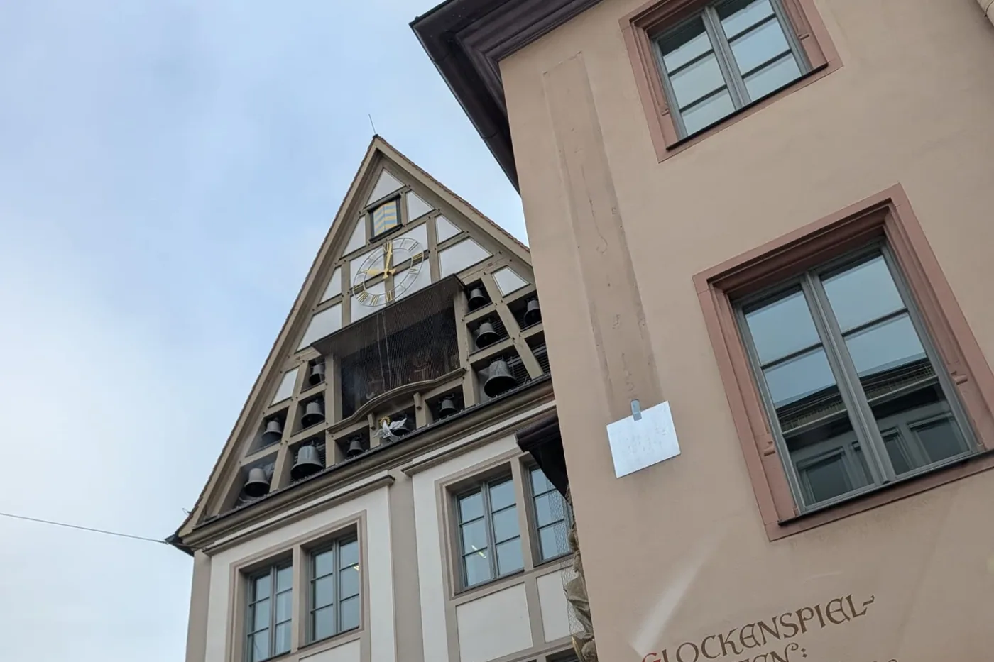 Der Giebel des Bürgerspitals mit Uhr, Glocken und der Drehbühne des Glockenspiels, daneben die Hauswand mit den Spielzeiten