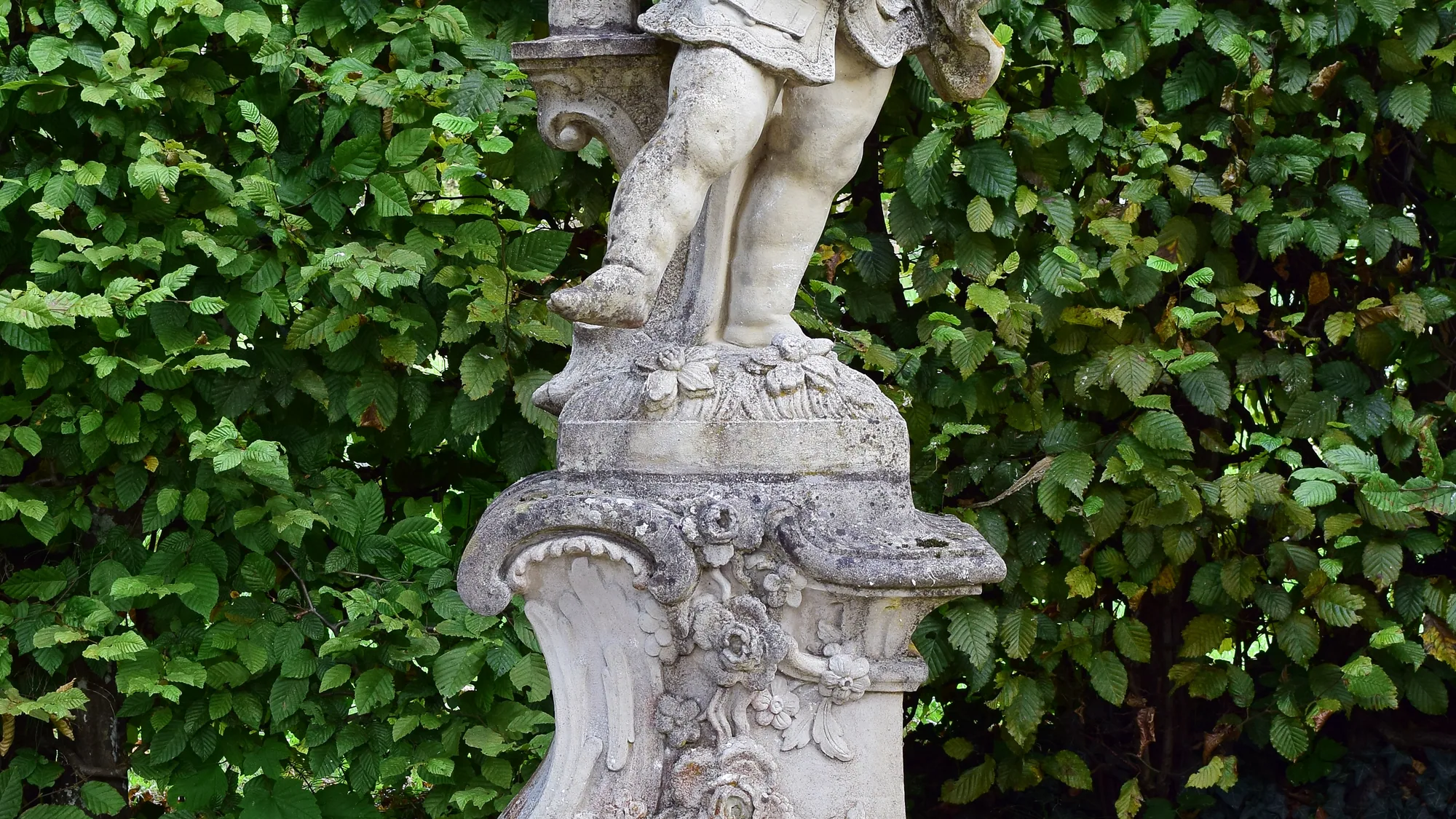 Puttenfigur aus Sandstein vor einer Hecke im Hofgarten Veitshöchheim