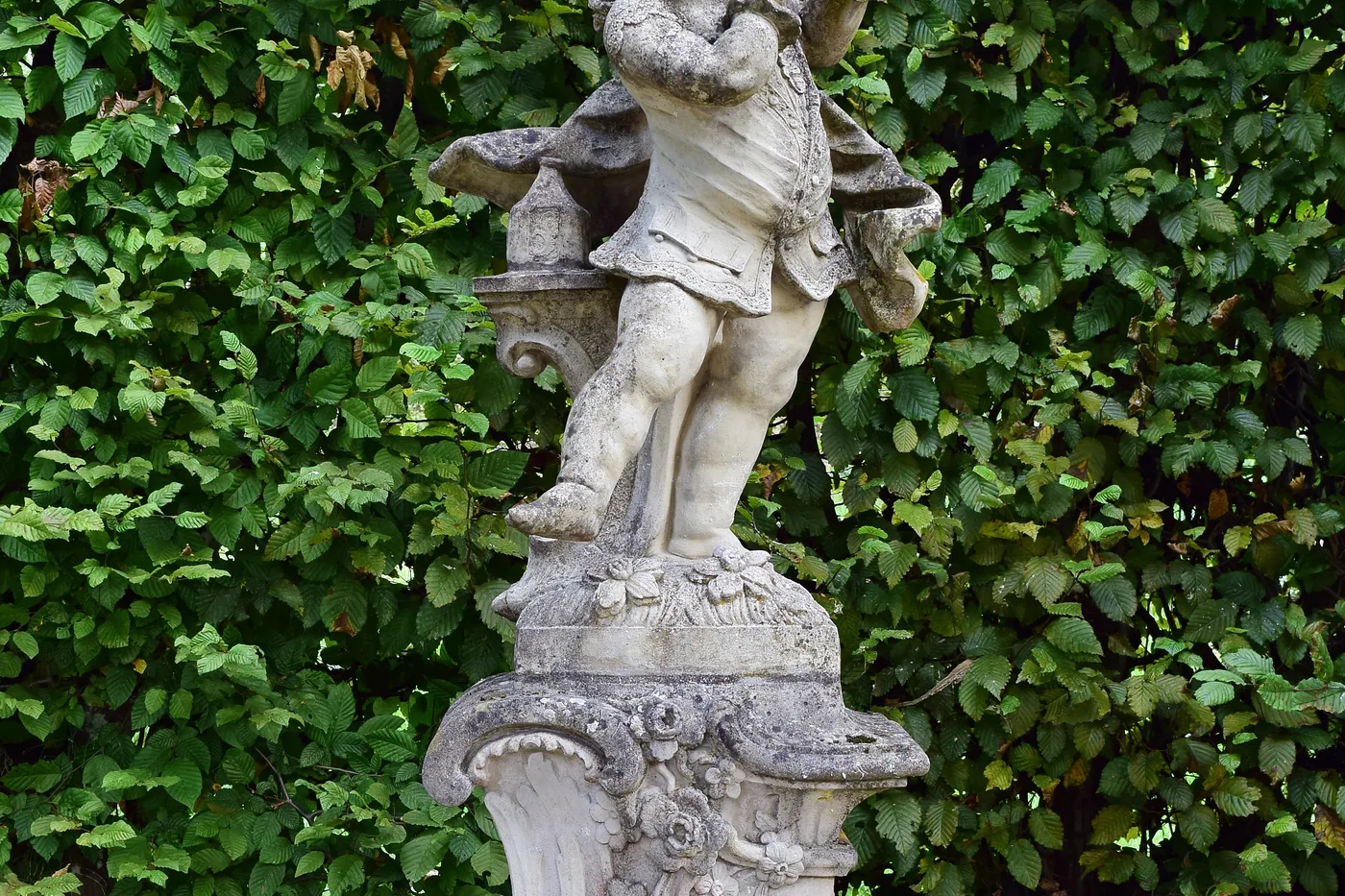 Puttenfigur aus Sandstein vor einer Hecke im Hofgarten Veitshöchheim