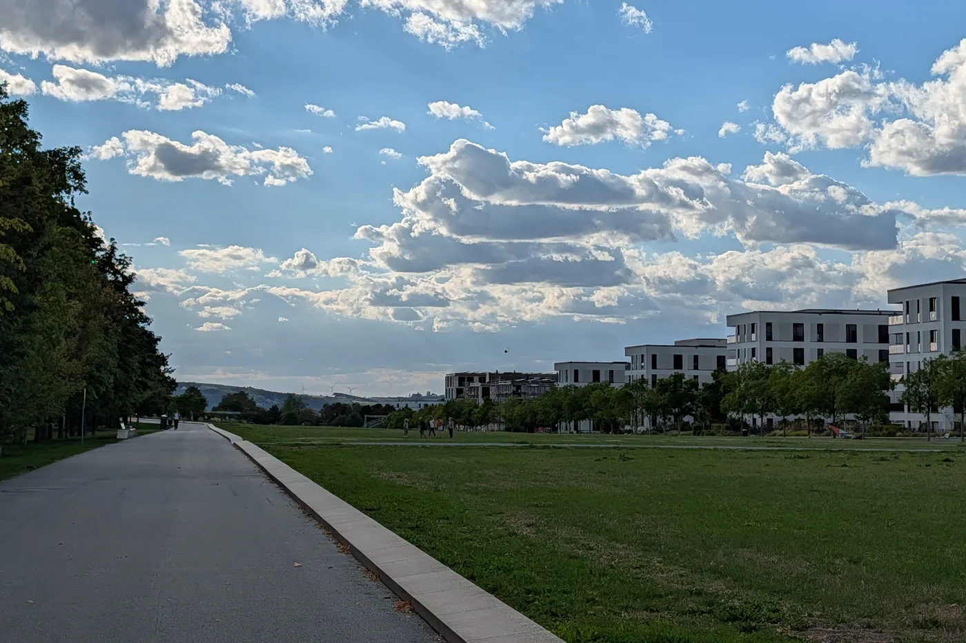 Ein breiter Weg am Rand der großen Wiese am Hubland, rechts die neue Wohnbebauung, am Horizont die Höhen westlich von Würzburg