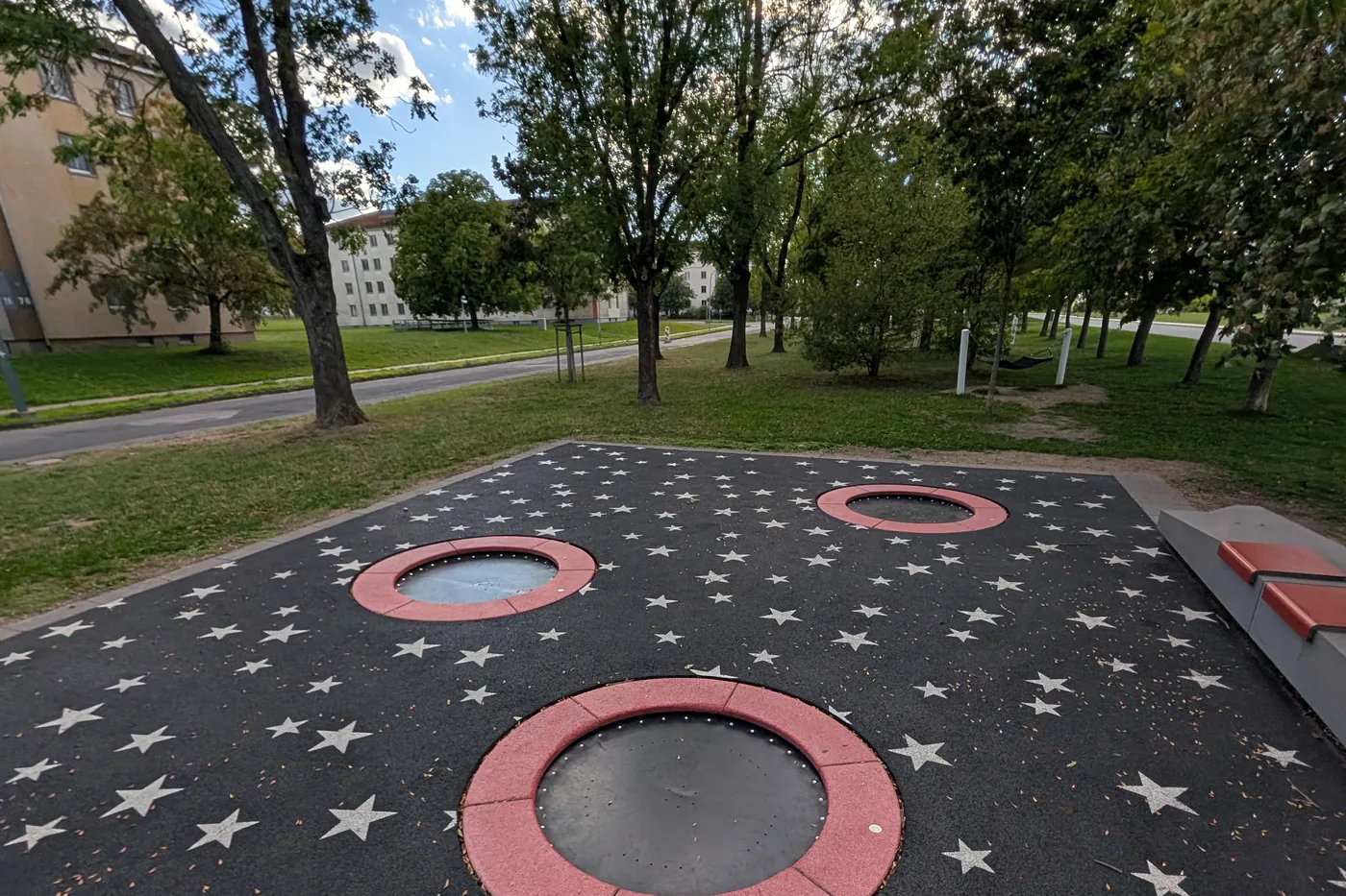 Drei in den Boden eingelassene Trampoline auf einer schwarzen Fläche mit aufgemalten weißen Sternen am Hubland, dahinter Gebäude der früheren Kaserne
