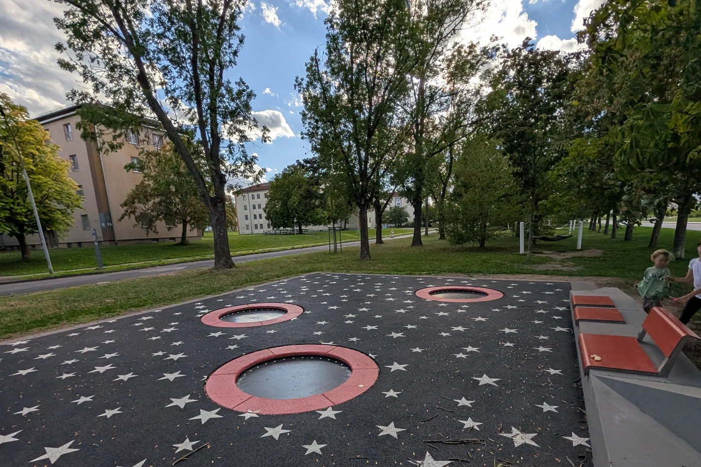 Die Trampolinfläche am Hubland mit Sitzbänken an der Seite, rechts spielen Kinder