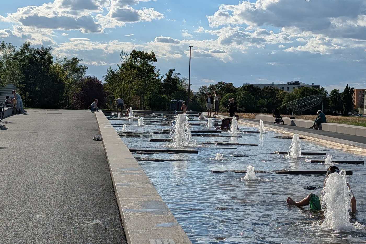 Kinder spielen in einem flachen Wasserbecken am Hubland, aus dem in einer langen Reihe Fontänen aufsteigen