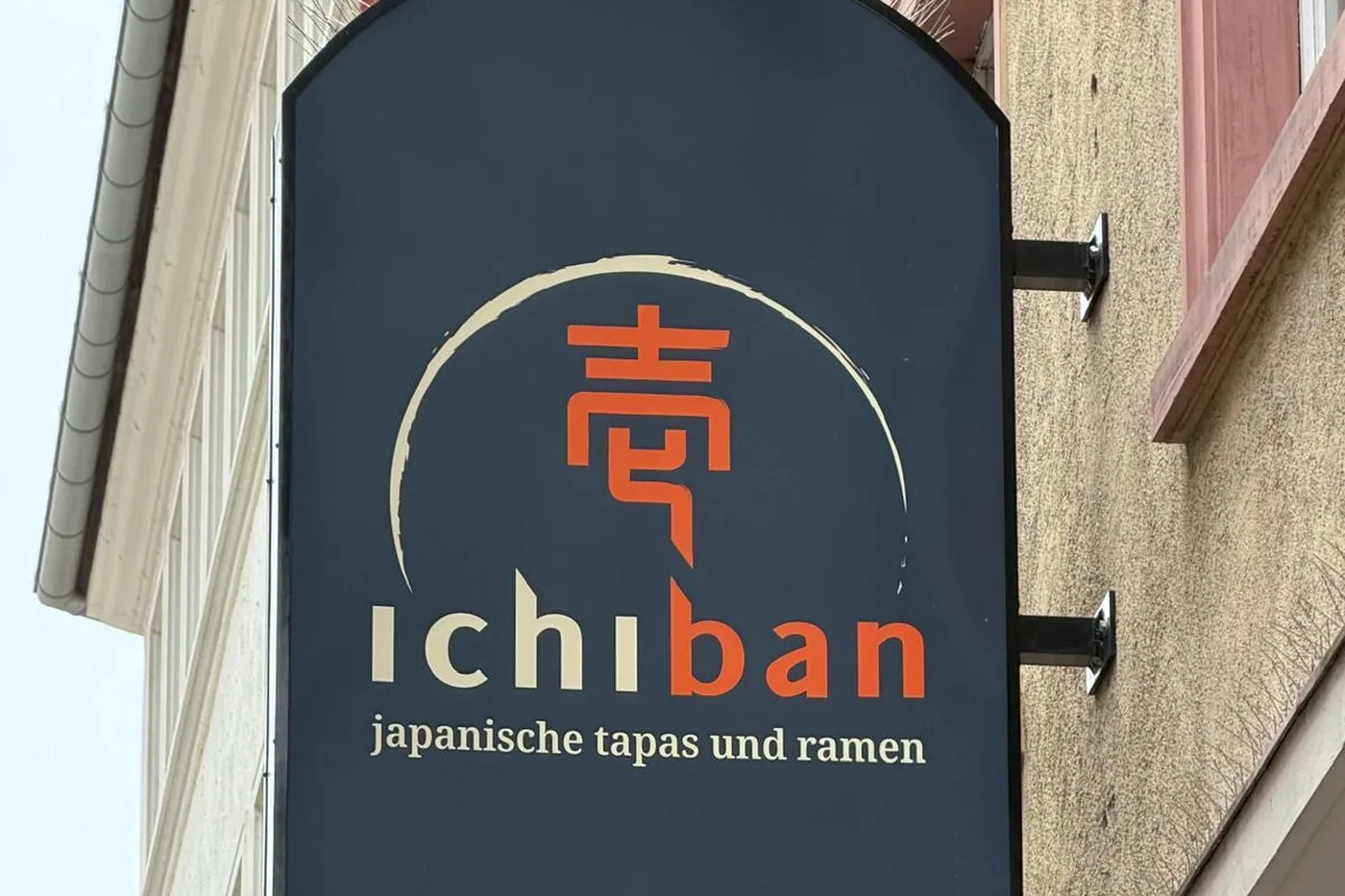 Das dunkelblaue Auslegerschild des Ichiban mit einem japanischen Schriftzeichen im Pinselkreis und der Zeile japanische tapas und ramen