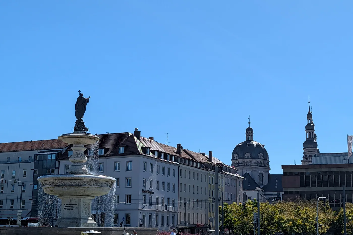Der Kiliansbrunnen vor dem Hauptbahnhof, dahinter die Kuppel des Stift Haug und die Daecher der Innenstadt