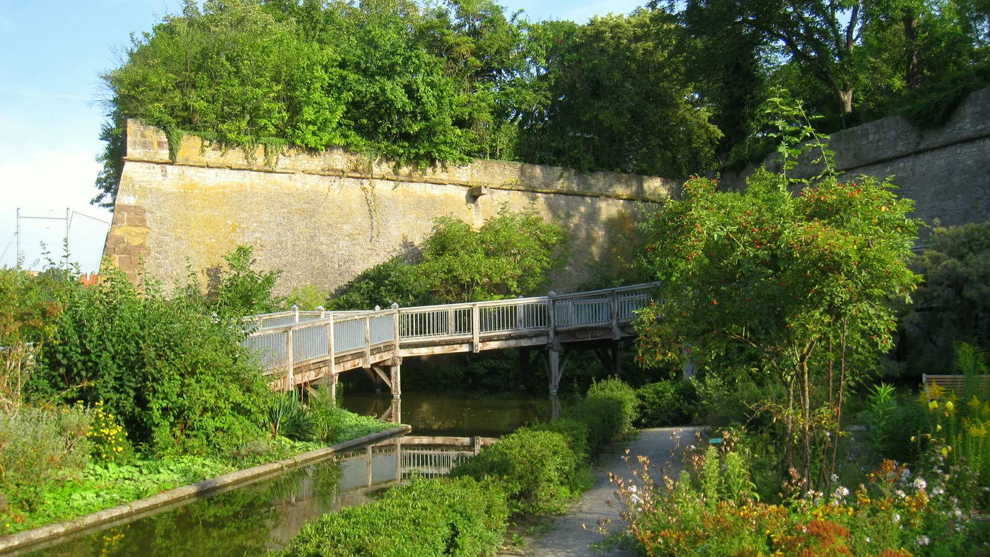 Wassergraben und Steg im Landesgartenschaupark, dahinter die Mauer des Festungsbergs