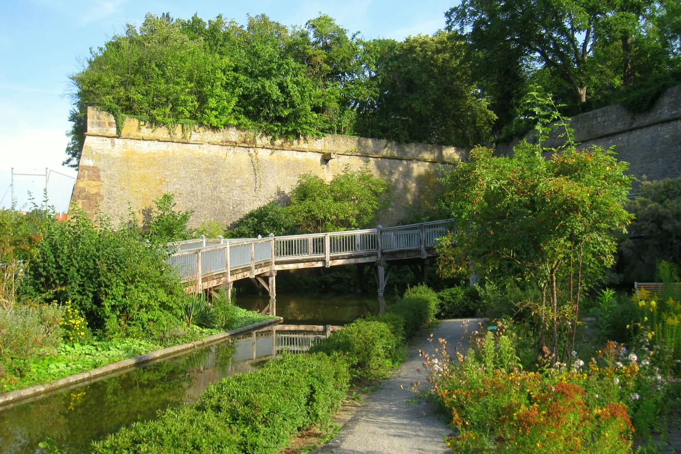 Wassergraben und Steg im Landesgartenschaupark, dahinter die Mauer des Festungsbergs