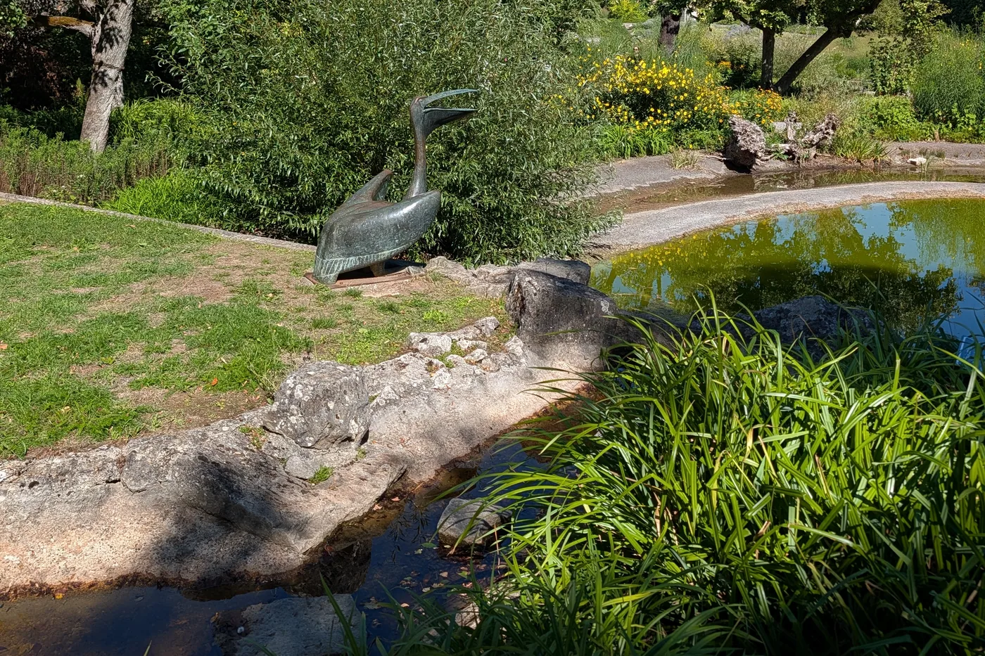 Eine Bronzeskulptur in Form eines Reihers am Rand des Teichs