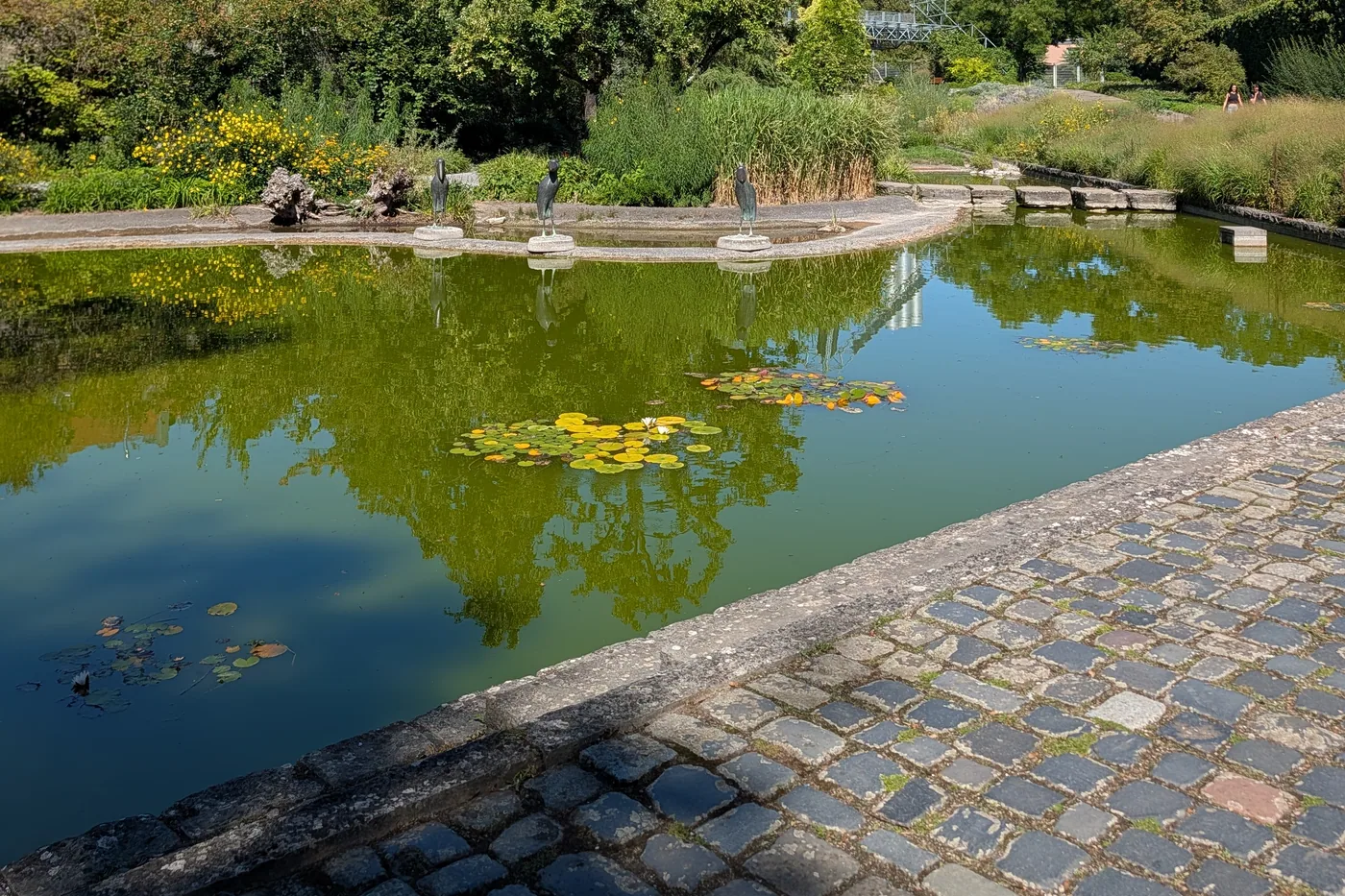 Der Teich mit Seerosen und drei Bronzefiguren auf Steinsockeln