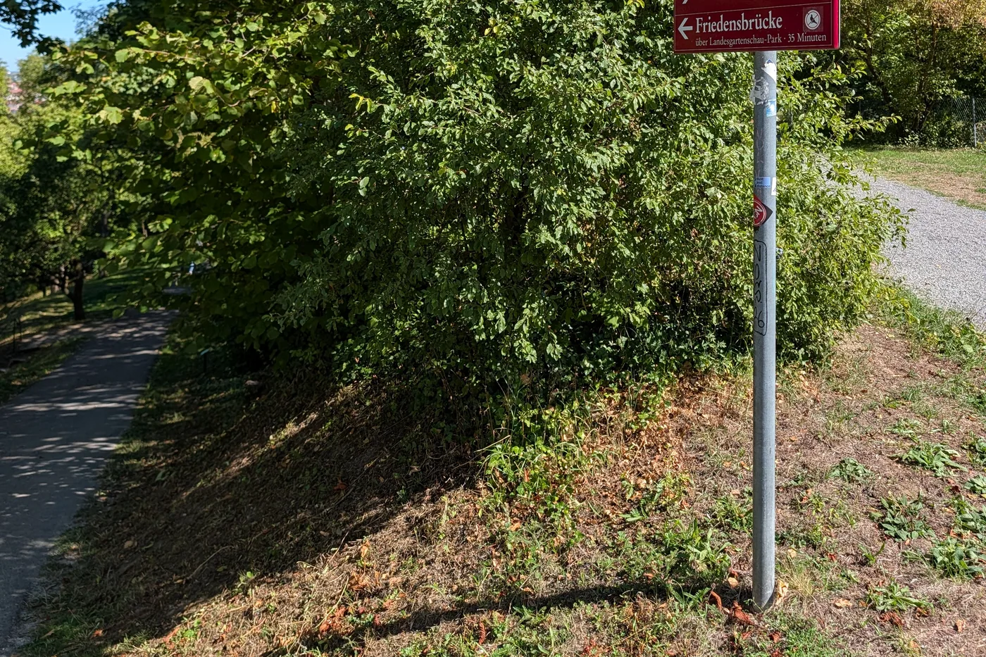 Ein Wegweiser im Park: rechts zur Festung Marienberg, links zur Friedensbrücke über den Landesgartenschau-Park, 35 Minuten