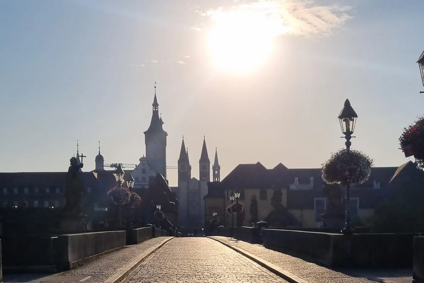 Das leere Kopfsteinpflaster der Alten Mainbrücke am frühen Morgen, die Sonne steht tief zwischen den Heiligenfiguren