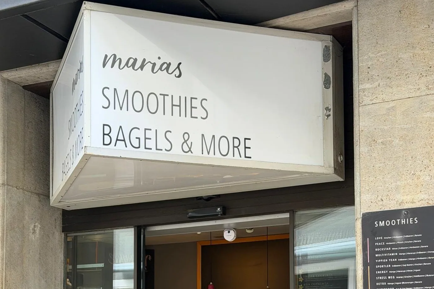Der weiße Leuchtkasten von marias Smoothies, Bagels & More über dem Eingang in der Wilhelmstraße, rechts die Tafel mit den Smoothie-Sorten