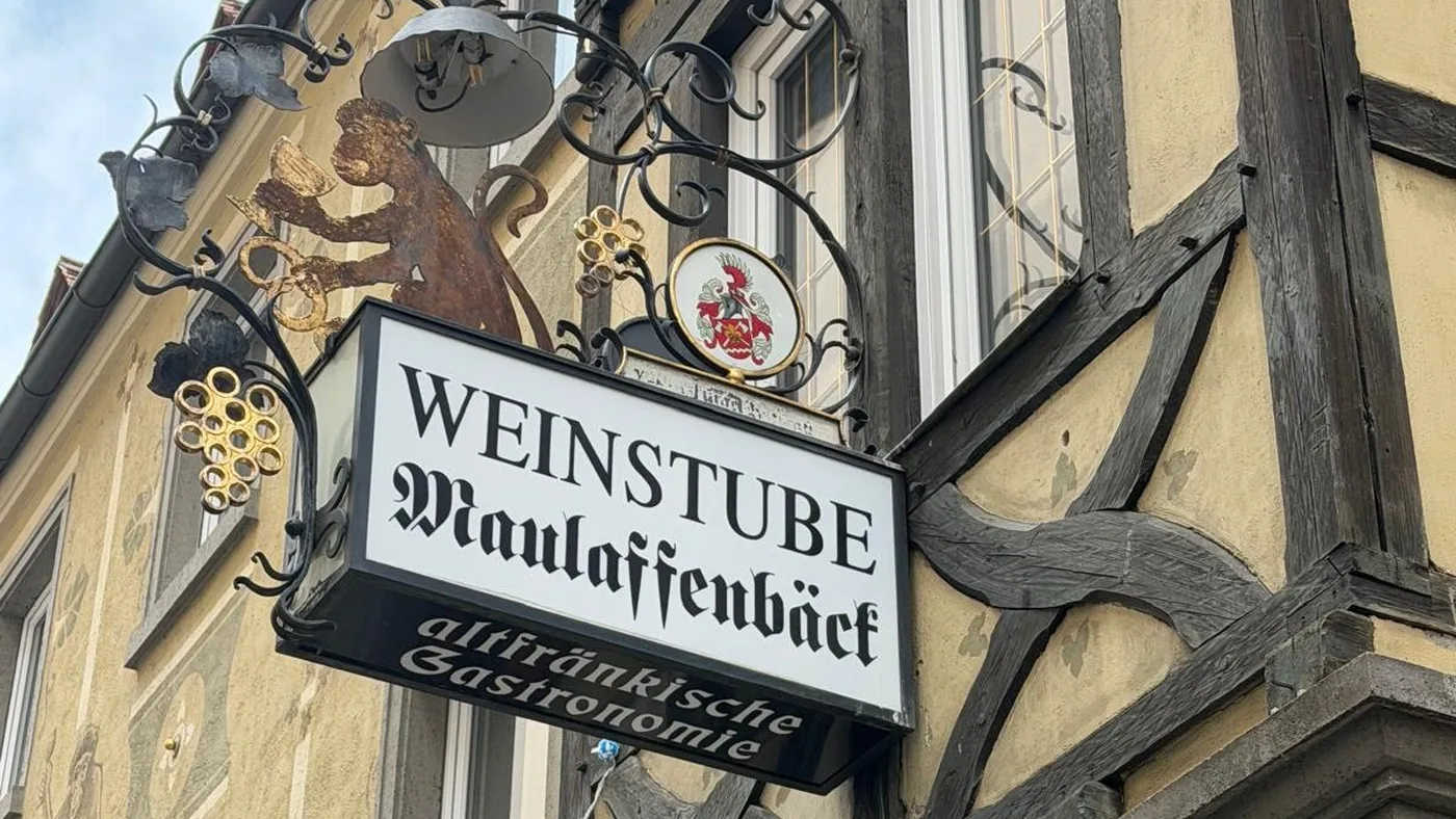Das schmiedeeiserne Wirtshausschild der Weinstube Maulaffenbäck mit dem lesenden Affen und dem Würzburger Wappen, am Fachwerk der Maulhardgasse