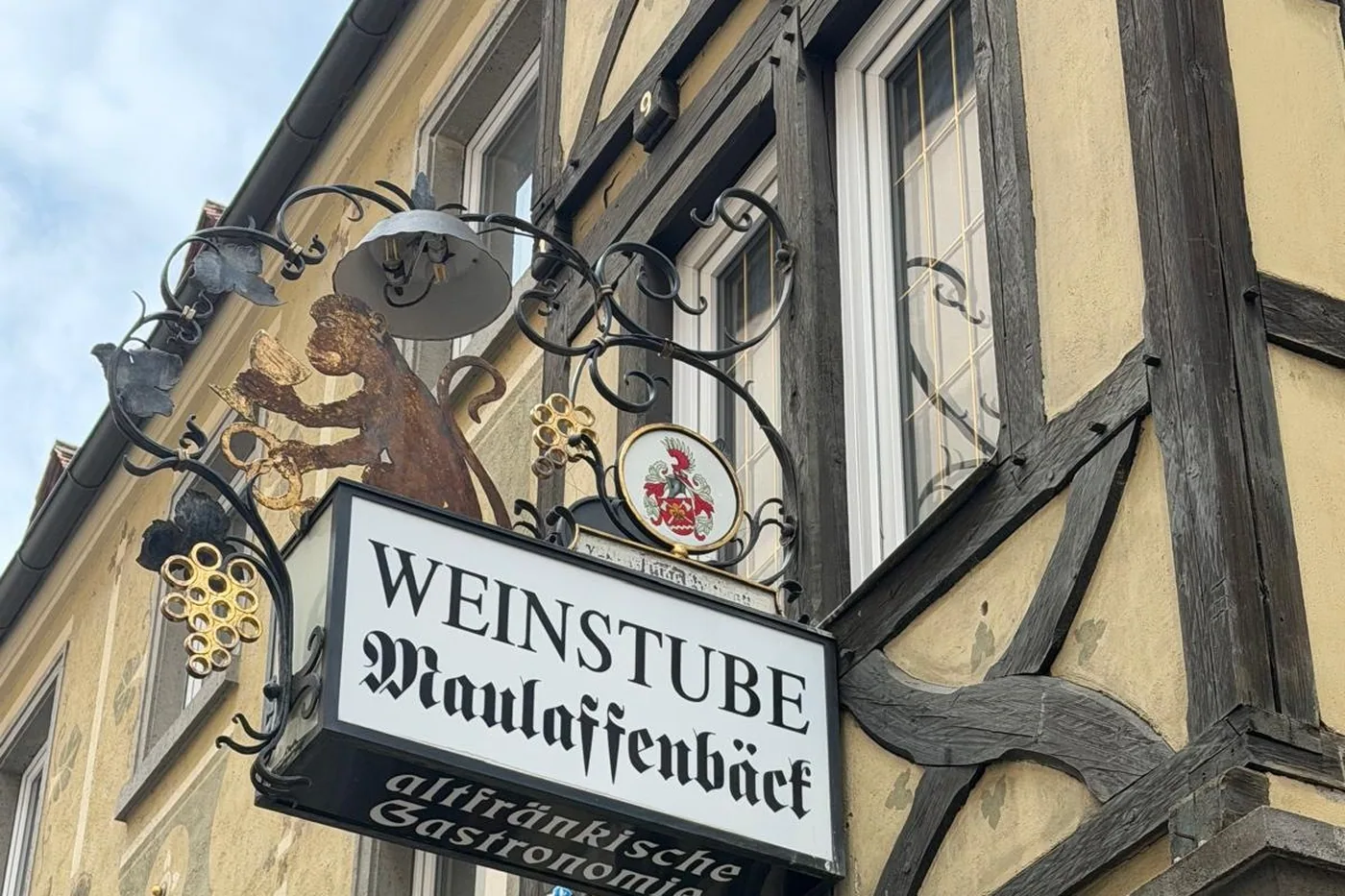 Das schmiedeeiserne Wirtshausschild der Weinstube Maulaffenbäck mit dem lesenden Affen und dem Würzburger Wappen, am Fachwerk der Maulhardgasse