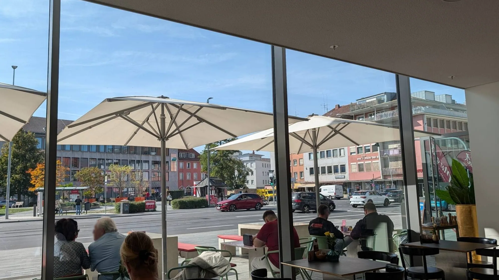 Blick aus dem Café Mozart durch die Glasfront auf die Terrasse mit weißen Sonnenschirmen und die Straße vor dem Mainfranken Theater