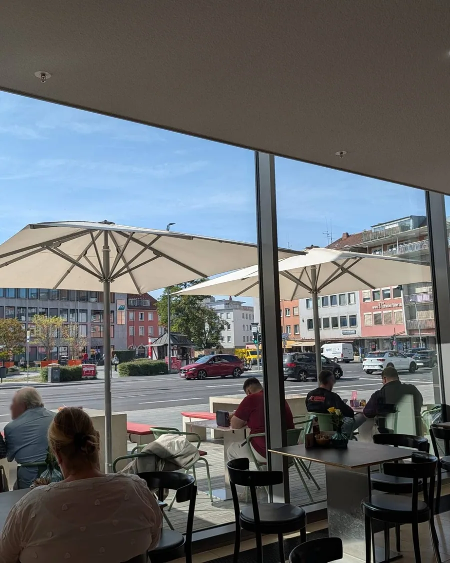 Blick aus dem Café Mozart durch die Glasfront auf die Terrasse mit weißen Sonnenschirmen und die Straße vor dem Mainfranken Theater