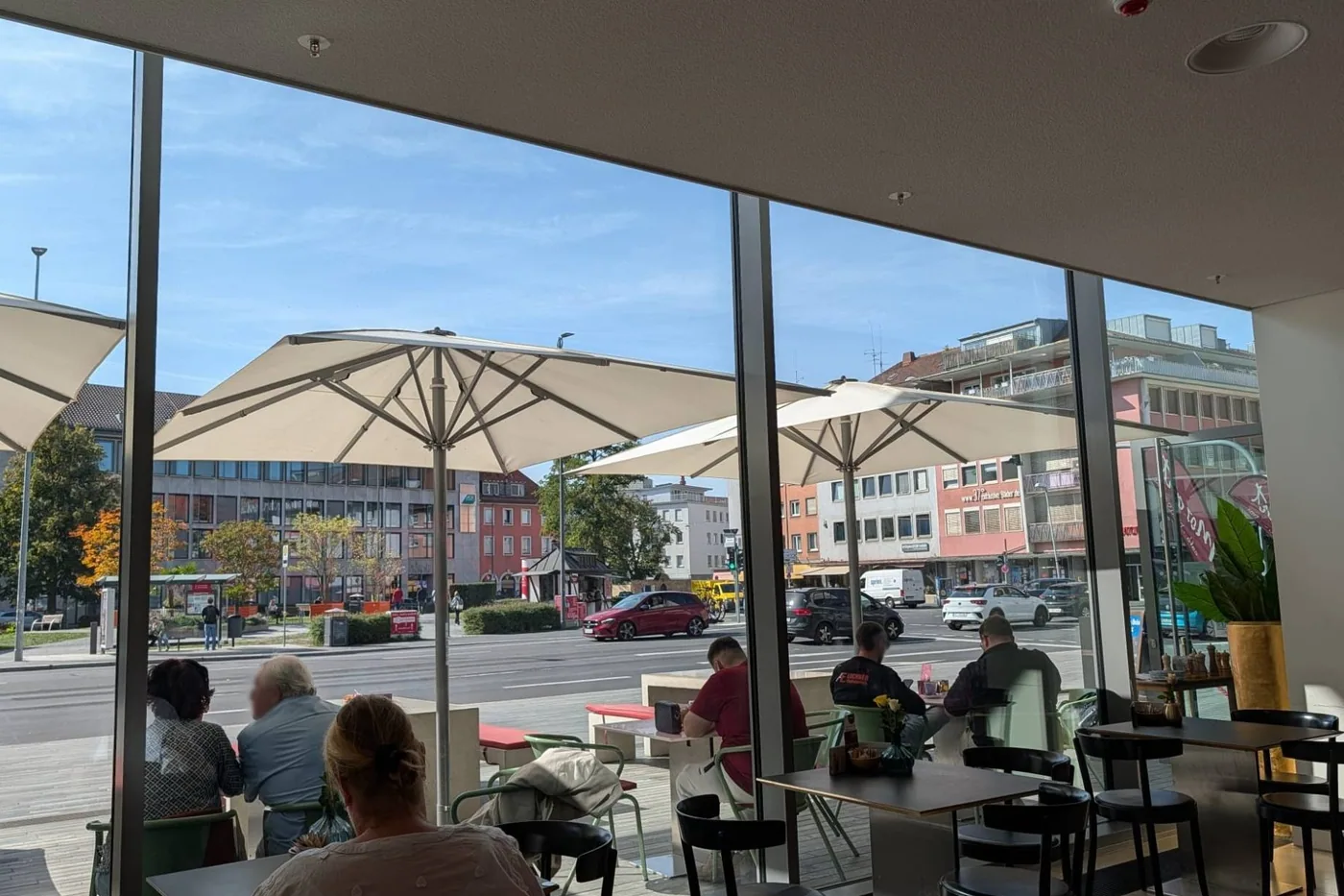 Blick aus dem Café Mozart durch die Glasfront auf die Terrasse mit weißen Sonnenschirmen und die Straße vor dem Mainfranken Theater