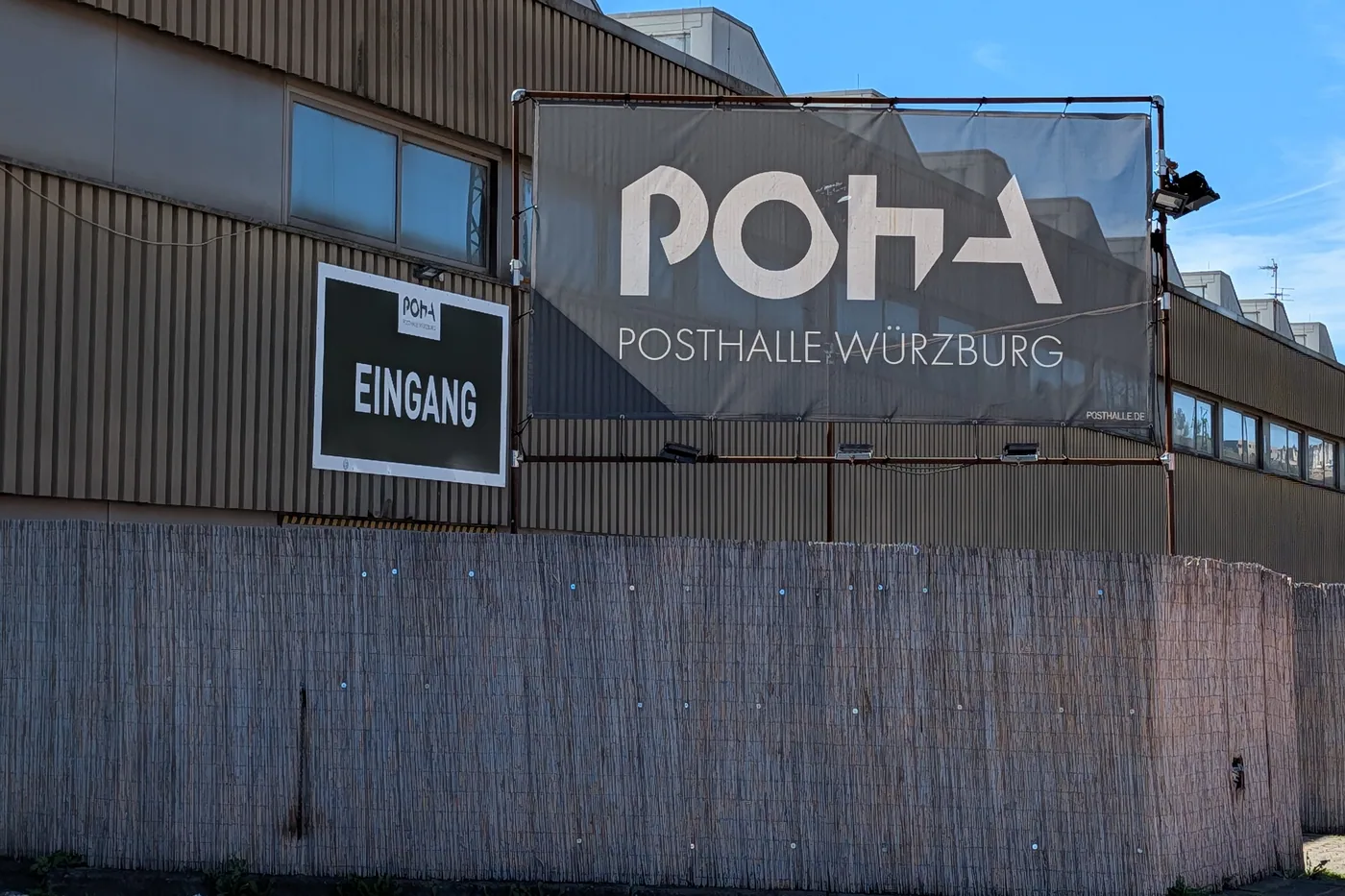 Das Banner mit dem POHA-Logo an der Wellblechfassade der Posthalle, links das Eingangsschild