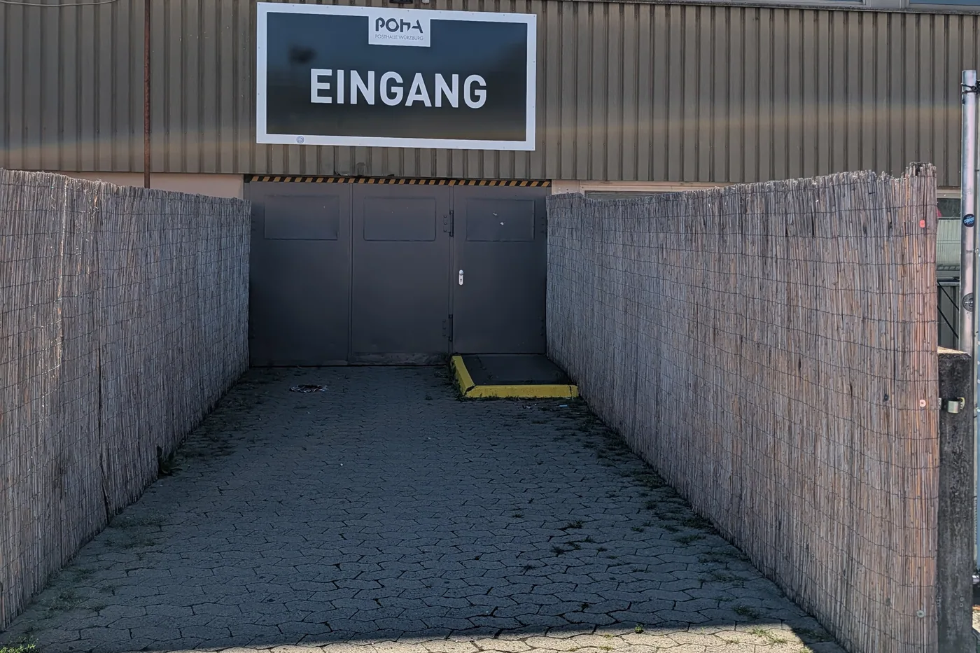 Der Eingang der Posthalle: eine Rampe zwischen Schilfmatten führt zum Tor unter dem Schriftzug Eingang