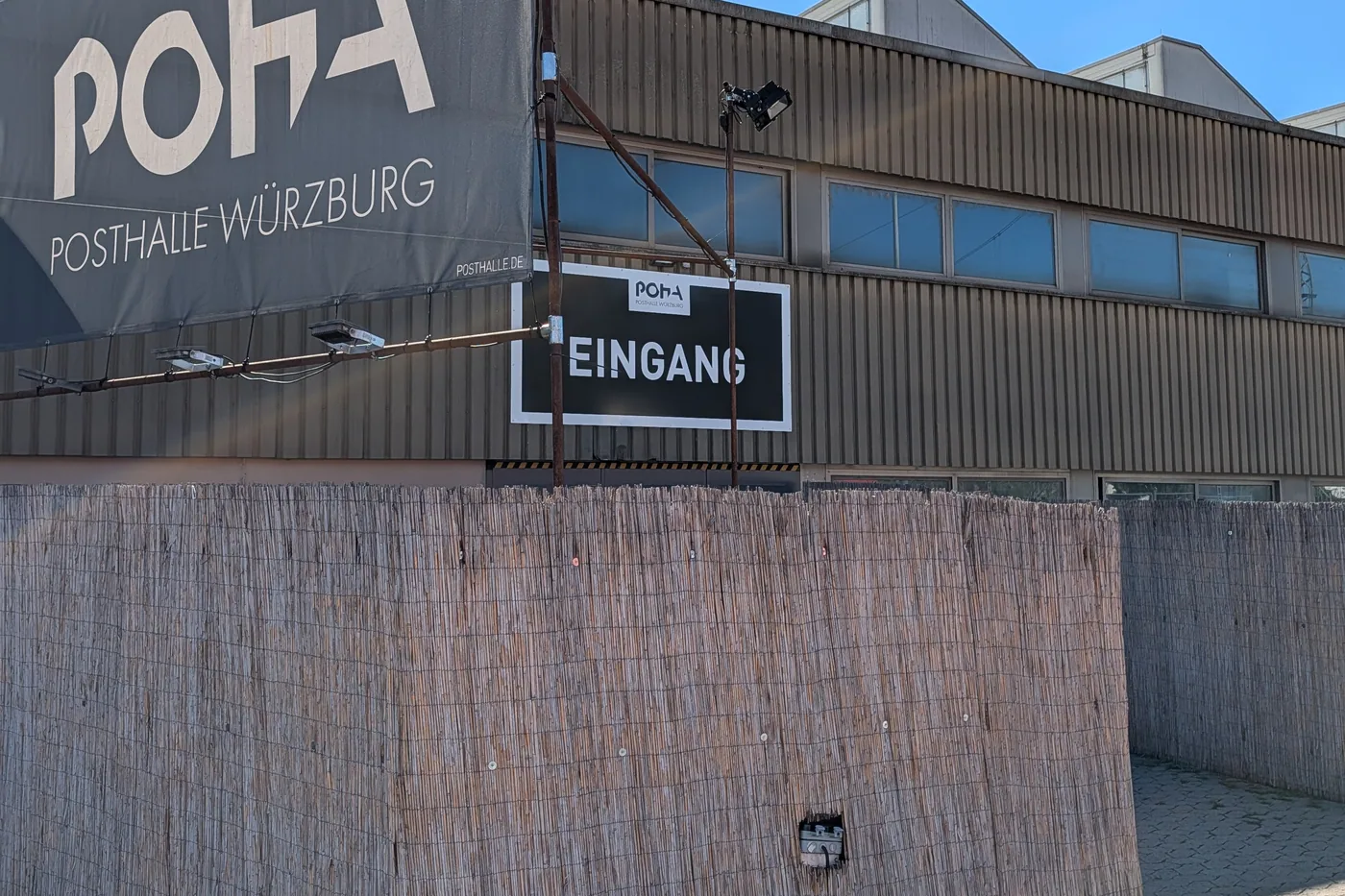 Die Posthalle von der Straße, das POHA-Banner über der Schilfmattenwand