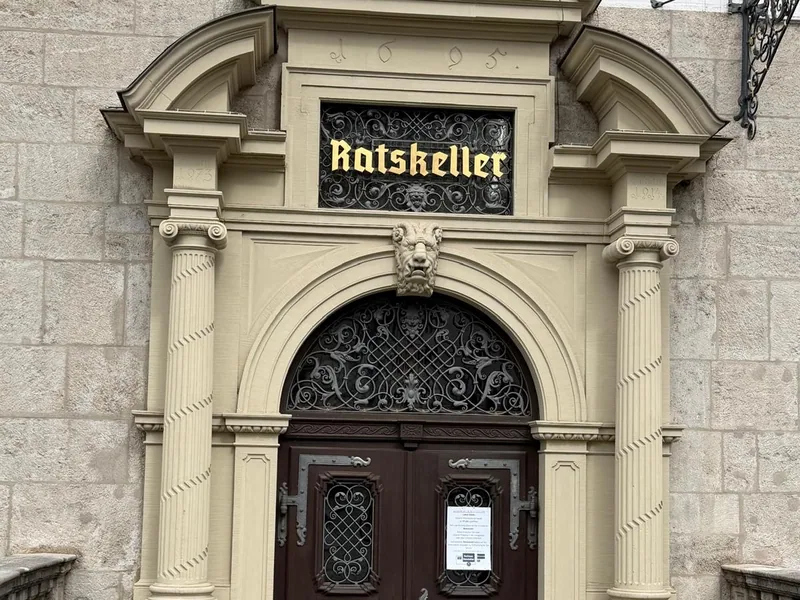 Das barocke Portal des Würzburger Ratskellers mit der Jahreszahl 1695 im Giebel, dem goldenen Schriftzug hinter Schmiedeeisen und einem Löwenkopf über dem Torbogen