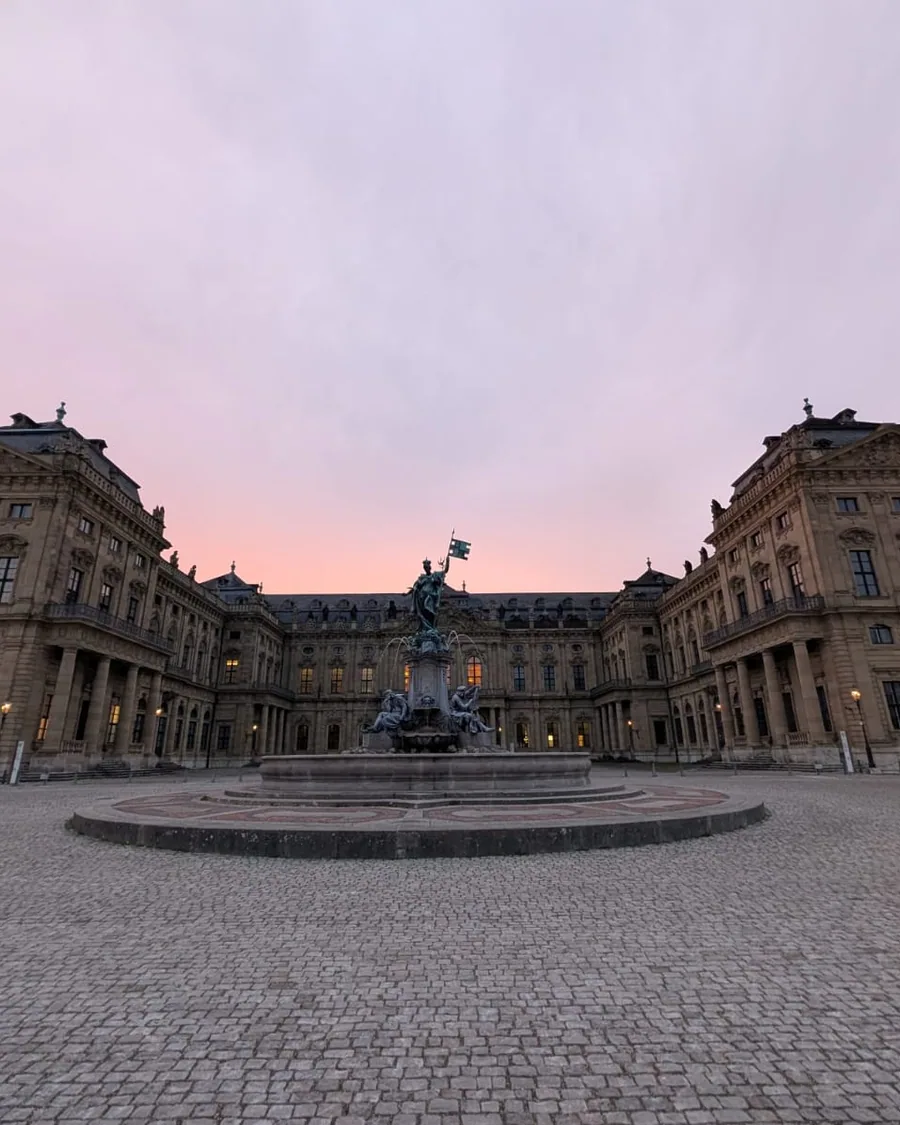 Der leere Residenzplatz im Morgenrot, in der Mitte der Frankoniabrunnen, dahinter die Flügel der Residenz um den Ehrenhof