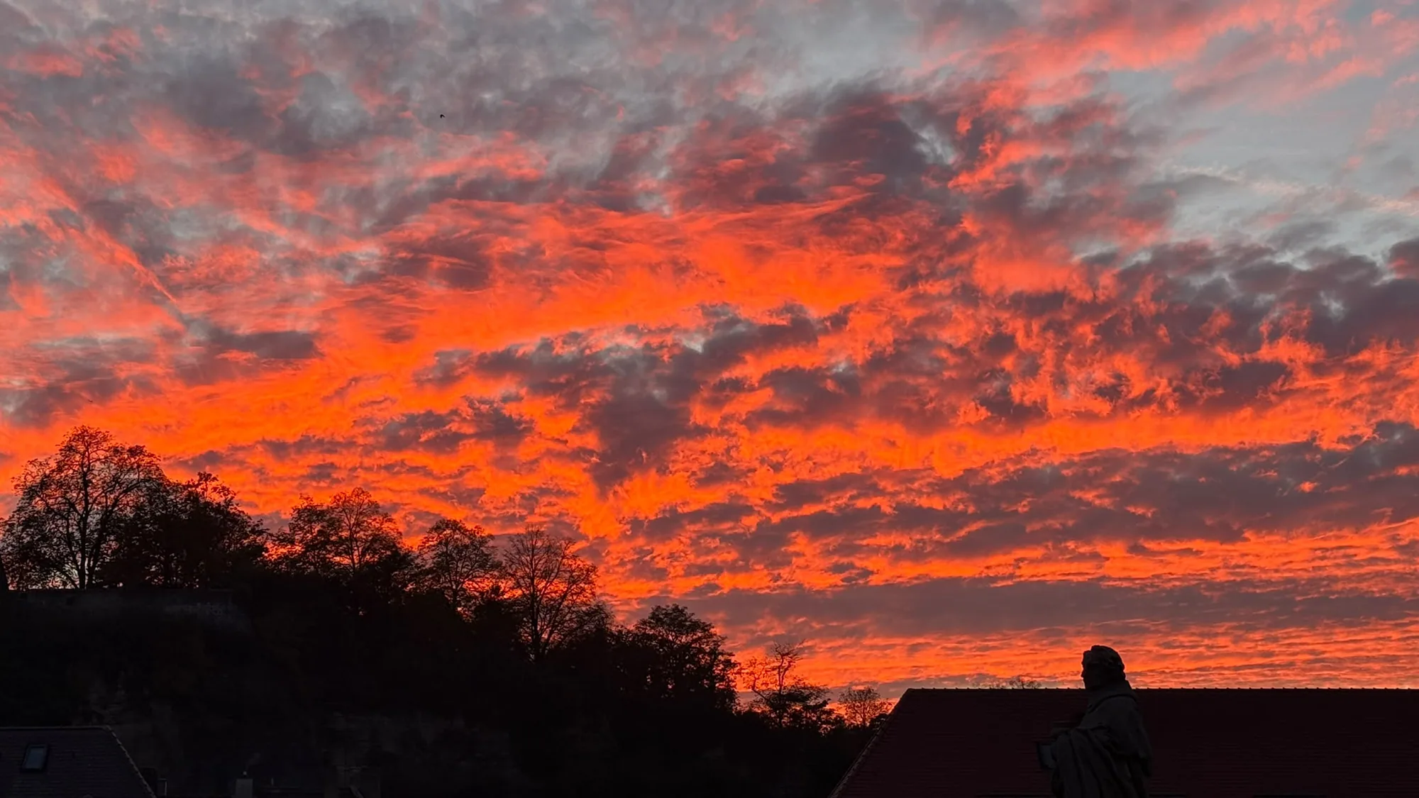 Glühend roter Abendhimmel über der Alten Mainbrücke, darunter der dunkle Hang des Marienbergs, Dächer und eine Brückenfigur als Umriss