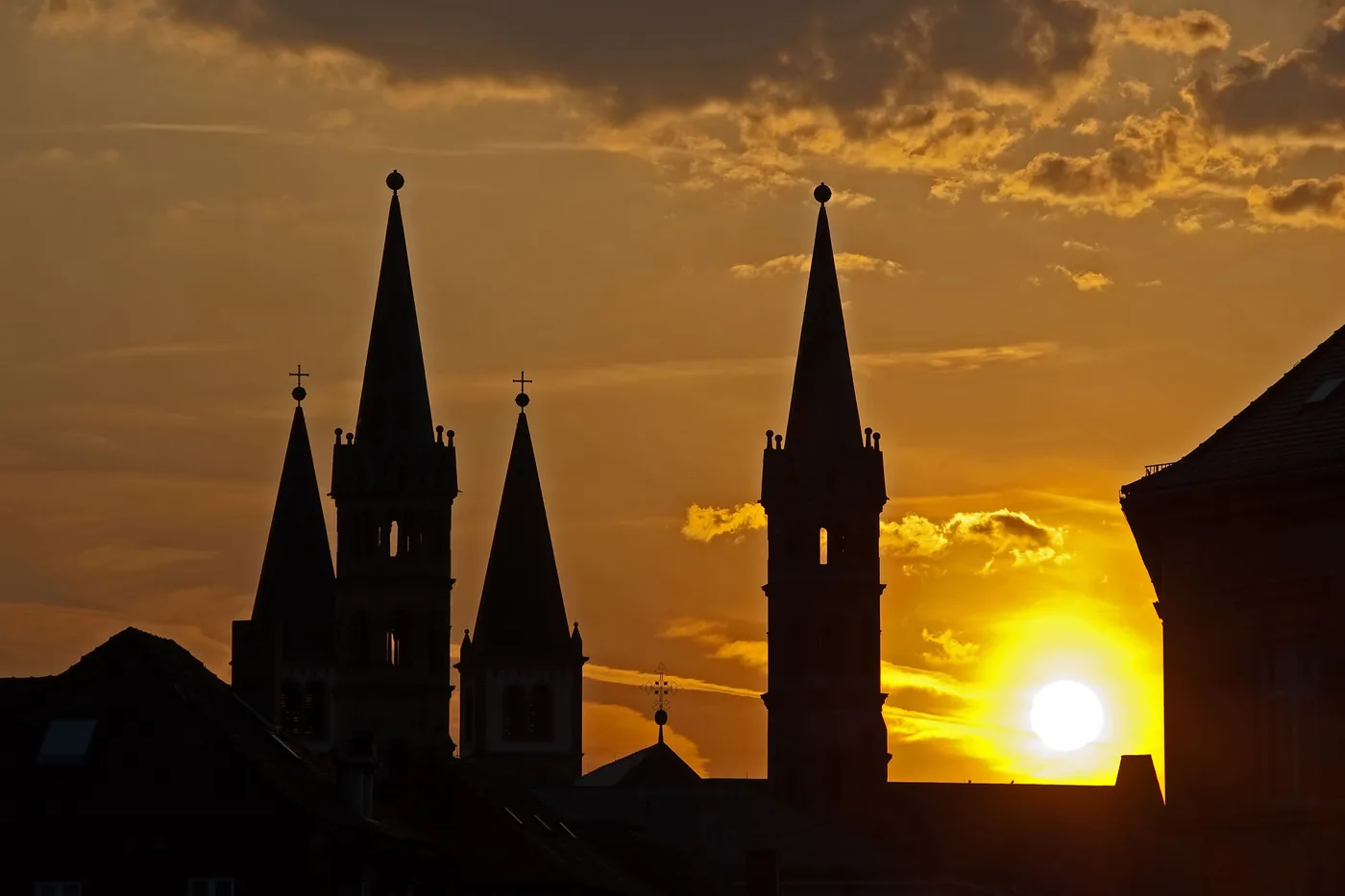 Kirchtürme der Würzburger Altstadt als dunkle Silhouette, rechts daneben sinkt die Sonne hinter ein Hausdach