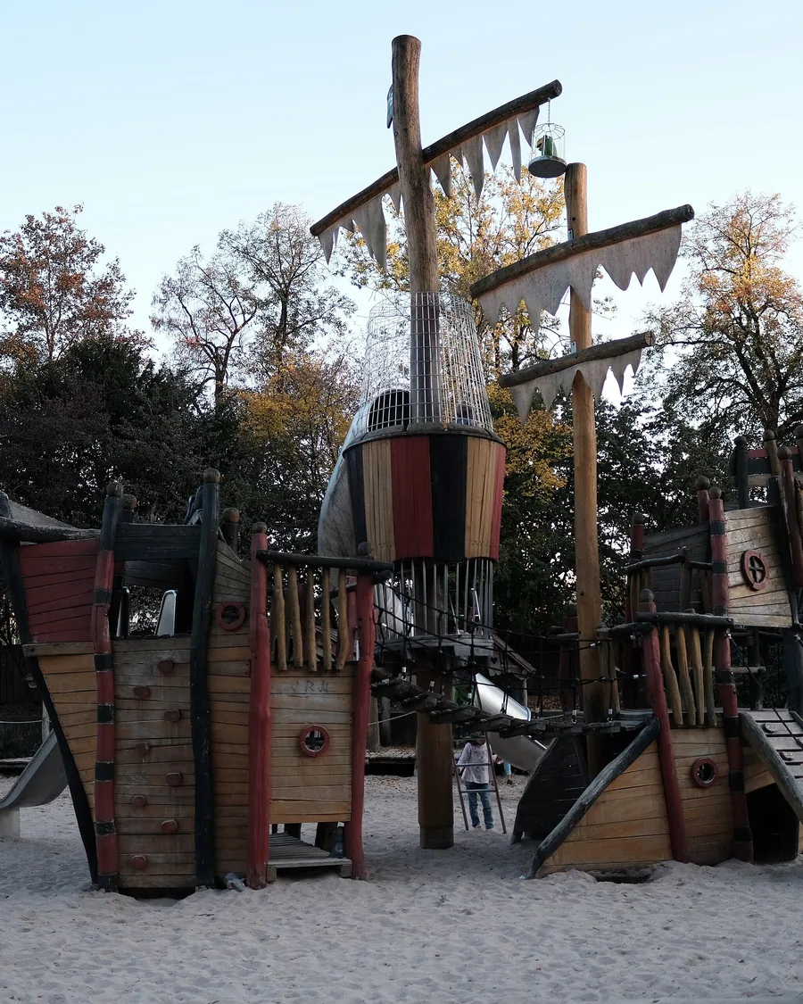 Kletterschiff aus Holz auf dem Piratenspielplatz, daneben ein Sandbereich