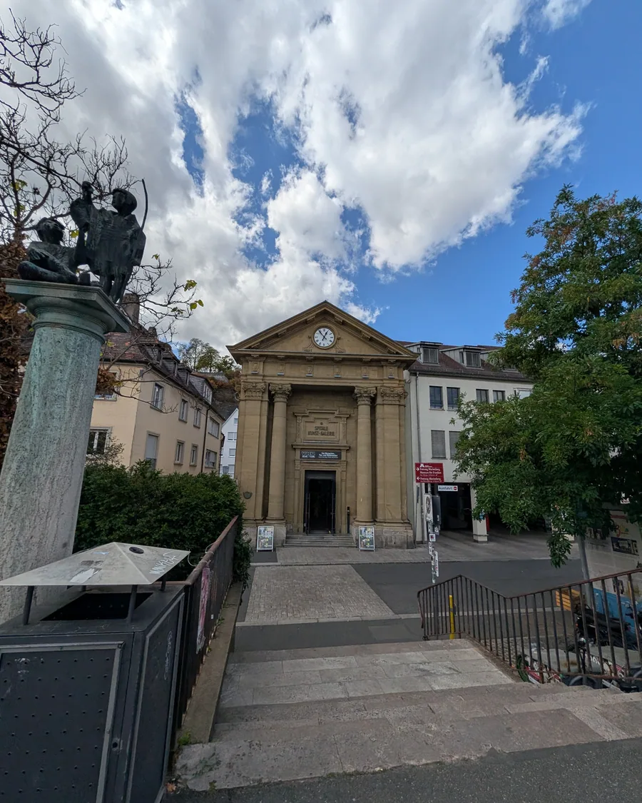 Das Spitäle am Mainufer mit Säulenportal und Uhr, davor die Skulptur auf der Säule