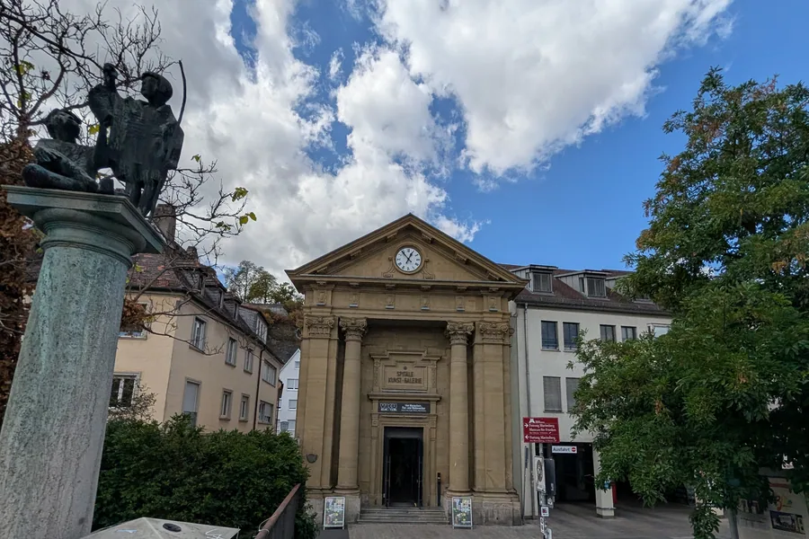 Das Spitäle am Mainufer mit Säulenportal und Uhr, davor die Skulptur auf der Säule