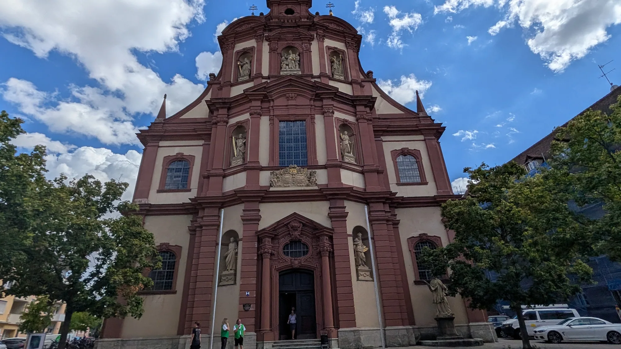 Die barocke Fassade der Kirche St. Peter und Paul in Würzburg, rot und weiß gefasst, mit Heiligenfiguren in Nischen über dem Portal