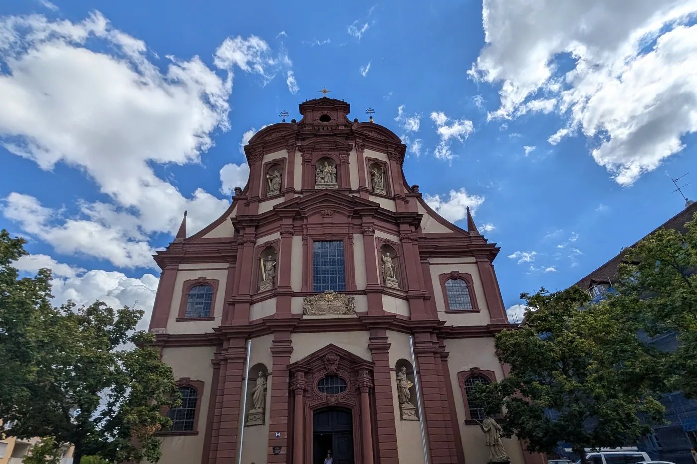 Die barocke Fassade der Kirche St. Peter und Paul in Würzburg, rot und weiß gefasst, mit Heiligenfiguren in Nischen über dem Portal