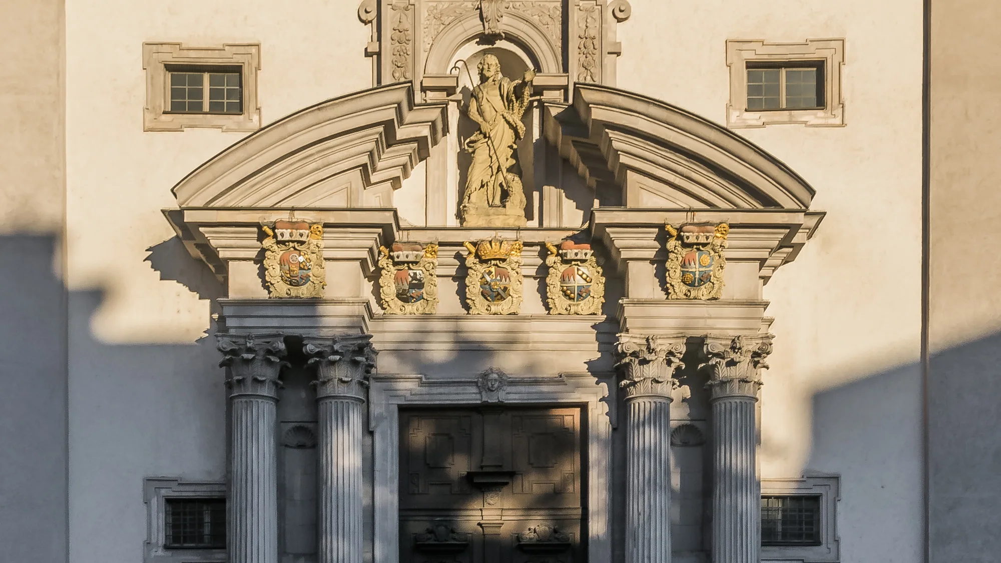Die Barockfassade von Stift Haug mit Figurennischen und Säulenportal, von der Straße aus gesehen