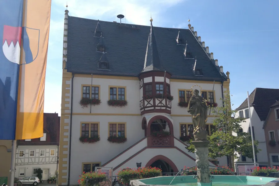 Das Rathaus von Volkach am Marktplatz, davor Brunnen und Fahne