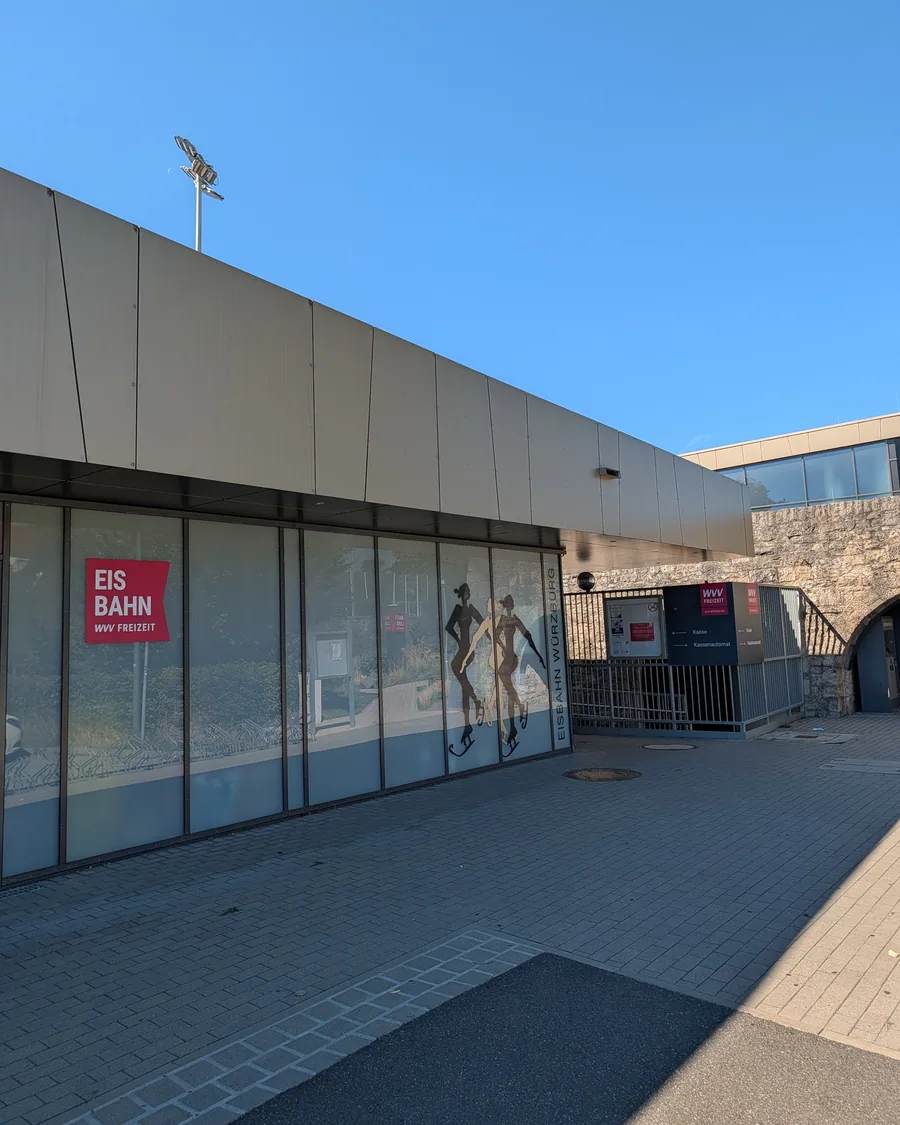 Der Eingang der Würzburger Eisbahn am Nigglweg, mit dem Schriftzug Eisbahn Würzburg und zwei Eisläuferinnen auf der Glasfassade