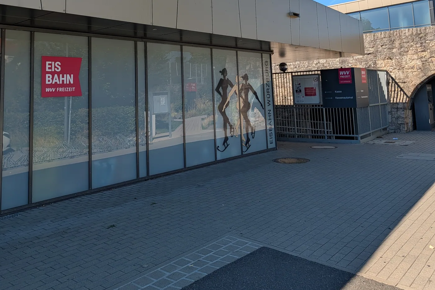 Der Eingang der Würzburger Eisbahn am Nigglweg, mit dem Schriftzug Eisbahn Würzburg und zwei Eisläuferinnen auf der Glasfassade