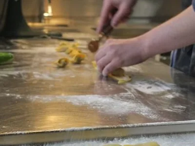 Hände formen gefüllte Teigtaschen auf einer bemehlten Arbeitsfläche