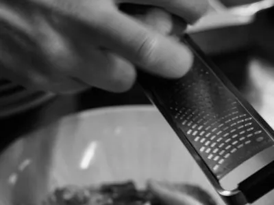 Über einem angerichteten Teller wird von Hand etwas gerieben, Schwarzweißaufnahme